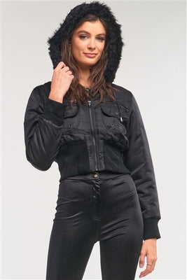 Image of a black bomber jacket that’s cropped at the midriff, features two breast pockets, a zipper closure, and a faux-fur drawstring hood.