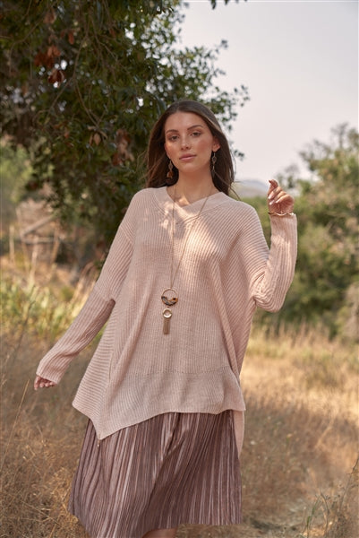 Image of a light pink, long-sleeve sweater with a v-neck line, asymmetrical hem, and gold zipper detail.