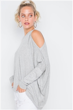 Charmed & Fortunate model wearing ladies’ apparel heather grey asymmetrical, cold-shoulder sweater with a scoop neck, the left shoulder cut out, and an asymmetrical hem.