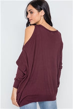 Charmed & Fortunate model wearing ladies’ apparel burnt copper asymmetrical cold-shoulder sweater with a scoop neck, the left shoulder cut out, and an asymmetrical hem.