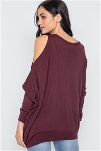 Charmed & Fortunate model wearing ladies’ apparel burnt copper asymmetrical cold-shoulder sweater with a scoop neck, the left shoulder cut out, and an asymmetrical hem.
